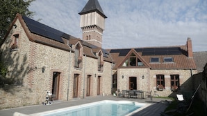 A stone building with a swimming pool, a tower, and solar panels.