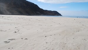 Una playa arenosa con huellas y una montaña al fondo.