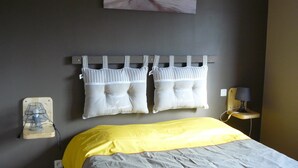 A bedroom with a bed, a bedside table with a lamp, a wall-mounted fan, and two pillows.