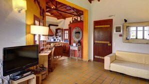 A cozy living room with a television, wooden furniture, a sofa, and a kitchen area with a red wall and wooden door. - Villa Kentavros Fully private pool villa away from it all! (Skopelos)