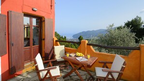 A balcony with wooden furniture and a table set with food, overlooking a scenic view of the sea and mountains. - Villa Kentavros Fully private pool villa away from it all! (Skopelos)