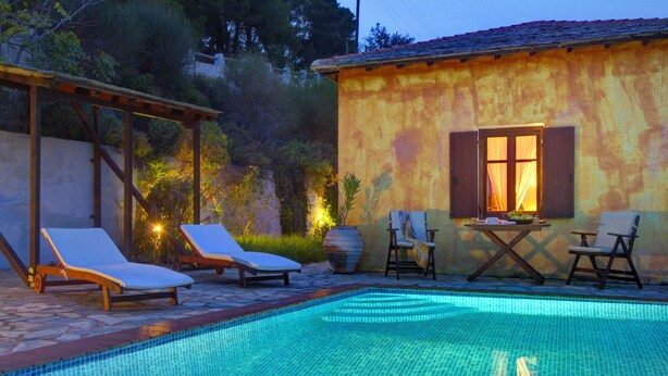 A swimming pool with lounge chairs and a table, surrounded by a garden and a building with a tiled roof. - Villa Kentavros Fully private pool villa away from it all! (Skopelos)