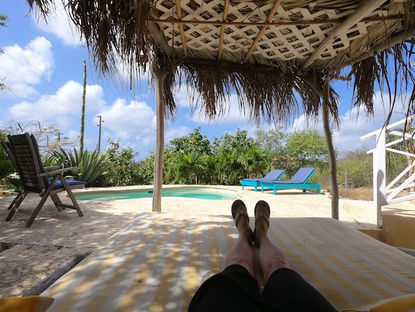A poolside area with a thatched roof, lounge chairs, and a clear view of the pool.