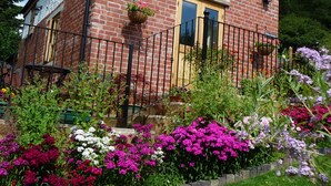 A brick house with a wooden door and window, surrounded by a metal fence and colorful flowers. - Secluded Detached Stable / Barn Conversion On The Border Of Shropshire And Wales (Oswestry Shropshire)