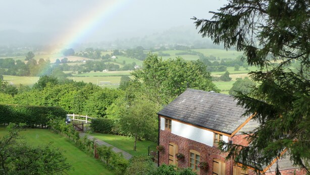 A house with a brick exterior and a sloped roof, surrounded by lush greenery and a view of a rural landscape. - Secluded Detached Stable / Barn Conversion On The Border Of Shropshire And Wales (Oswestry Shropshire)