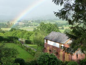 A house with a brick exterior and a sloped roof, surrounded by lush greenery and a view of a rural landscape. - Secluded Detached Stable / Barn Conversion On The Border Of Shropshire And Wales (Oswestry Shropshire)