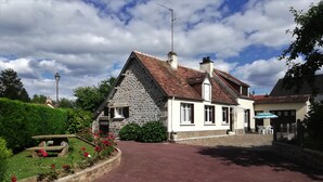 Une maison en pierre avec un toit recouvert de tuiles rouges, un mur en pierre et une allée pavée.