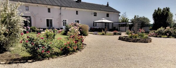 A white building with a gravel driveway, surrounded by well-maintained gardens and a covered outdoor seating area.