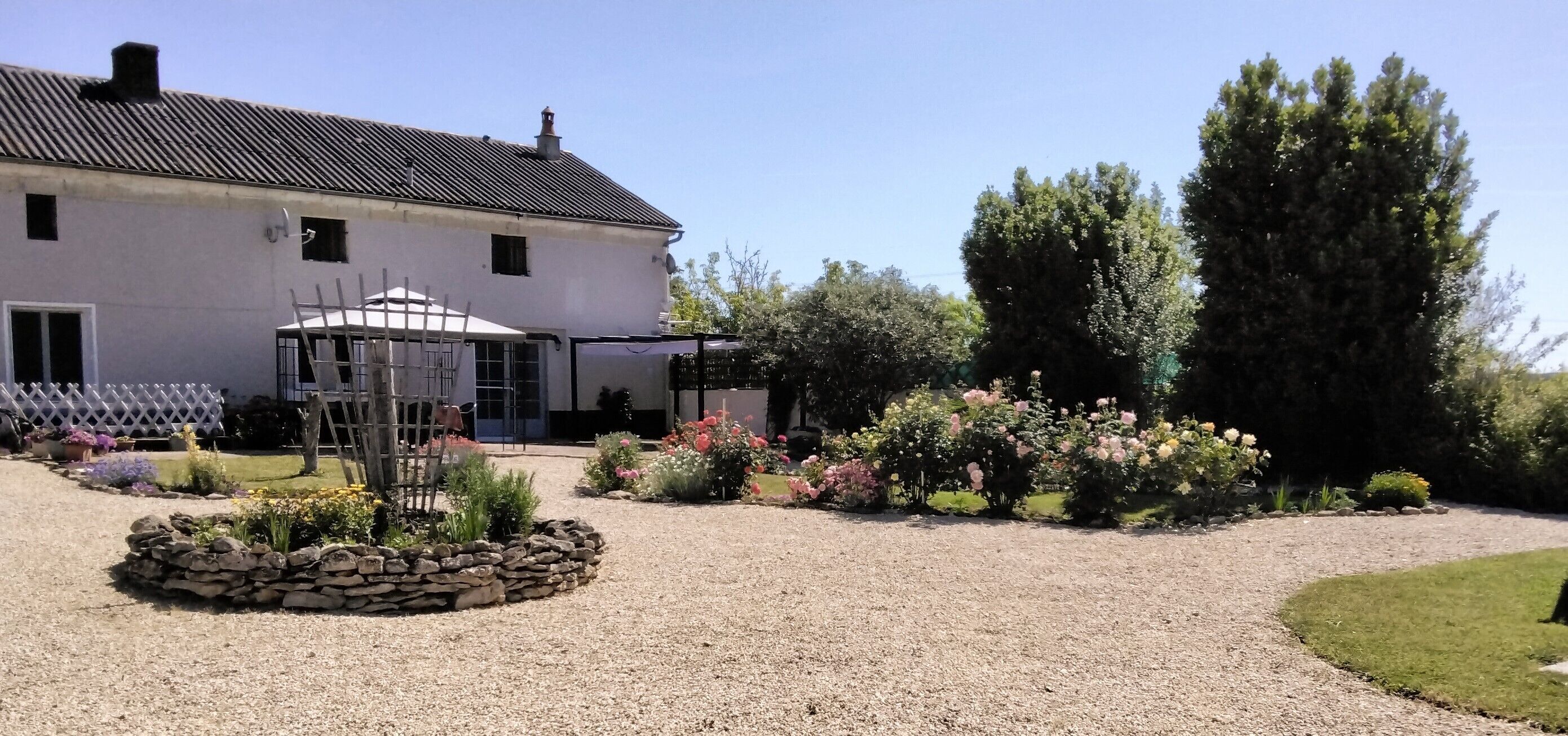 A white building with a gravel driveway and a garden with various plants and flowers.