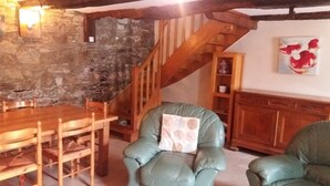 A rustic interior with a stone wall, wooden staircase, a dining table with chairs, and a green armchair with a pillow. - Le Cosquer farm (Saint-Connec)