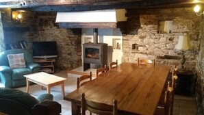 A rustic interior with a stone wall, a wooden table, and a television. - Le Cosquer farm (Saint-Connec)