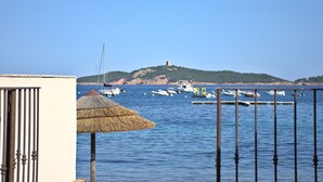 Une vue côtière avec des bateaux amarrés dans une marina, une construction à toit de chaume et, au loin, une colline surmontée d’une tour.