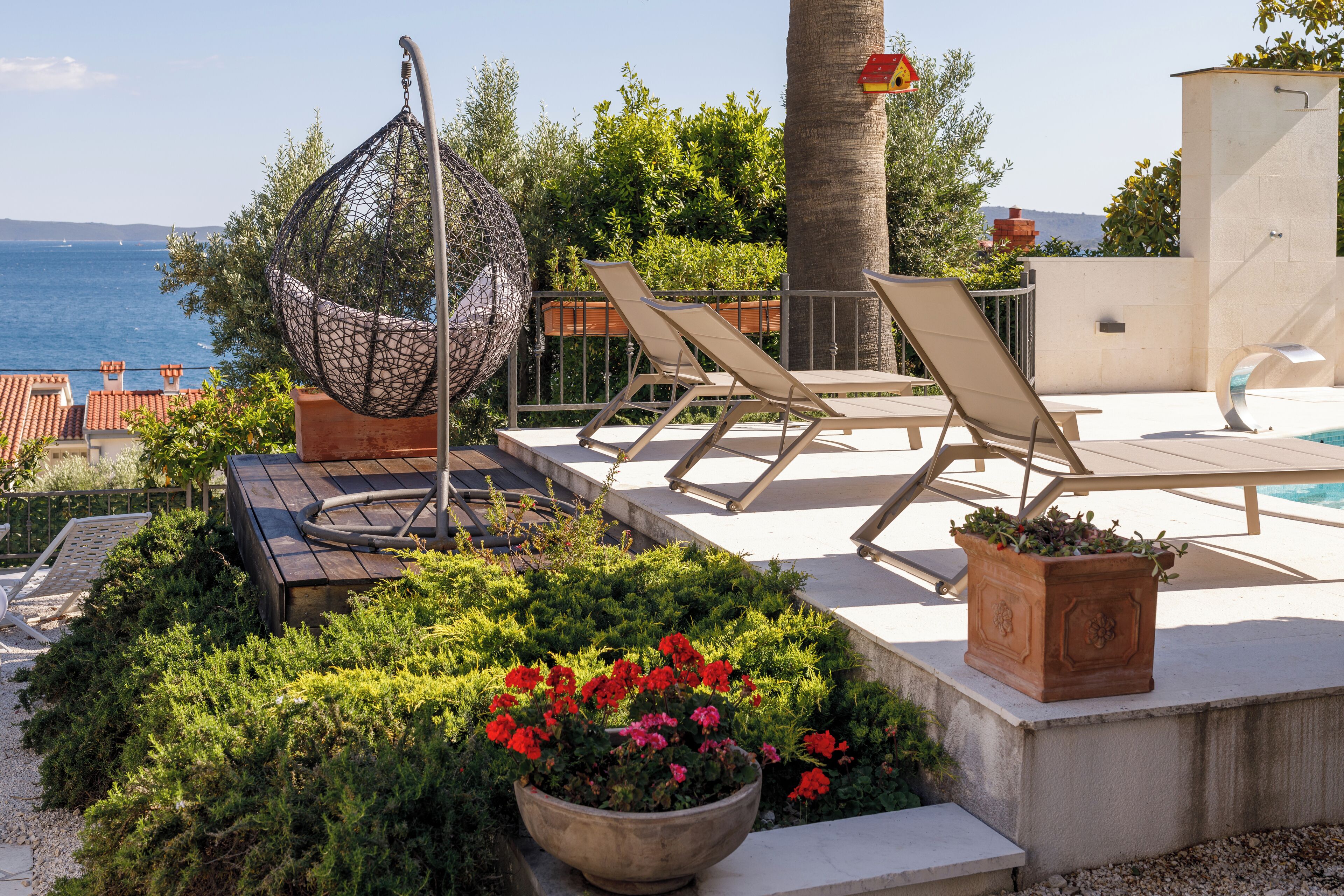 Una terraza con una silla colgante, sillones de descanso, una piscina y vistas al mar.