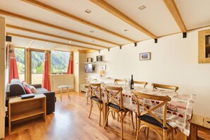 A cozy room with a wooden dining table, chairs, a sofa, and a TV. - Résidence Grand Roc - Campanules 311, Argentière (Chamonix), France (Argentière (Chamonix))