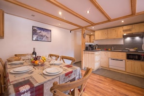 Un comedor con una mesa dispuesta para cuatro, una cocina con armarios de madera y un cuadro en la pared.