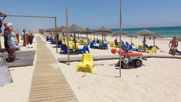 Una playa con filas de tumbonas y sombrillas, un paseo marítimo de madera y una vista despejada del mar.