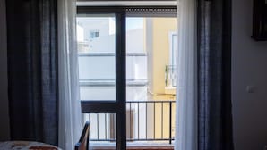 Una habitación con una cama, un ventanal con cortinas y vistas a un balcón con barandilla.