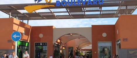 La entrada a ZENIA BOULEVARD, con un cartel claro, una pasarela peatonal y un letrero que indica 'SALIDA'.