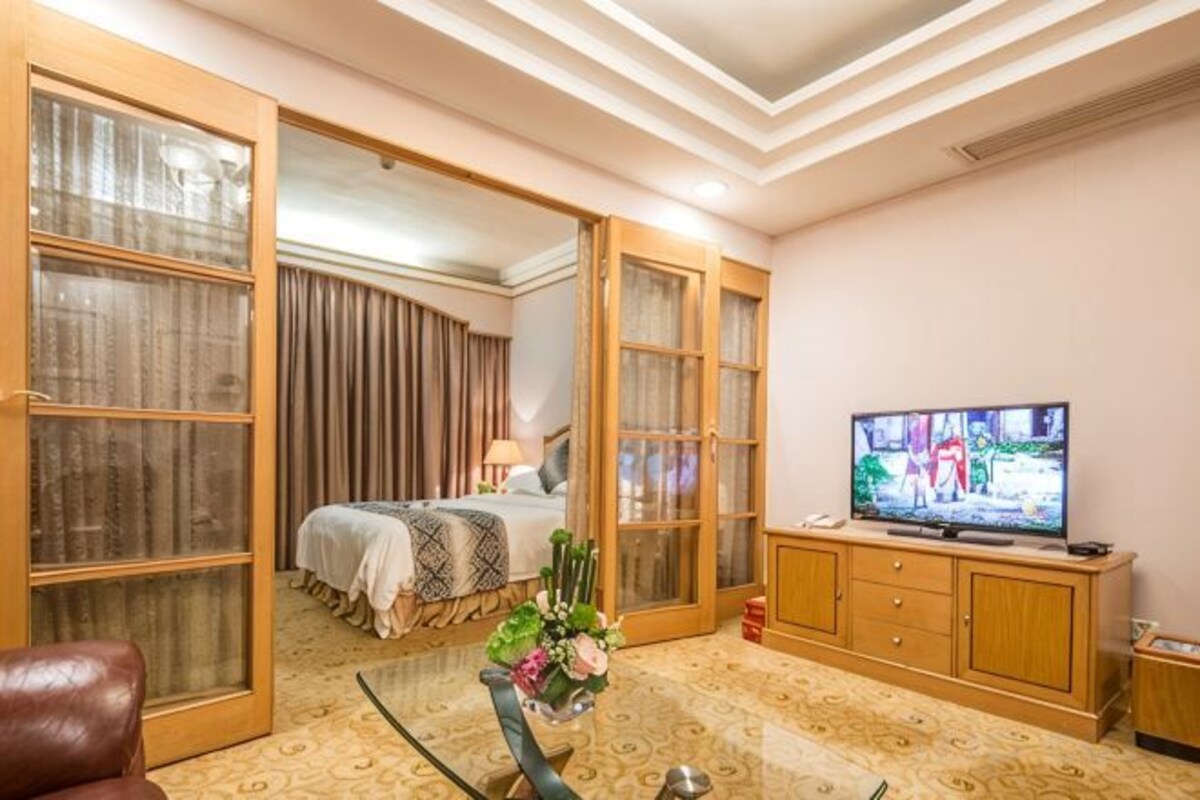 A hotel room with a bed, a television, a glass coffee table with flowers, and a wooden cabinet.