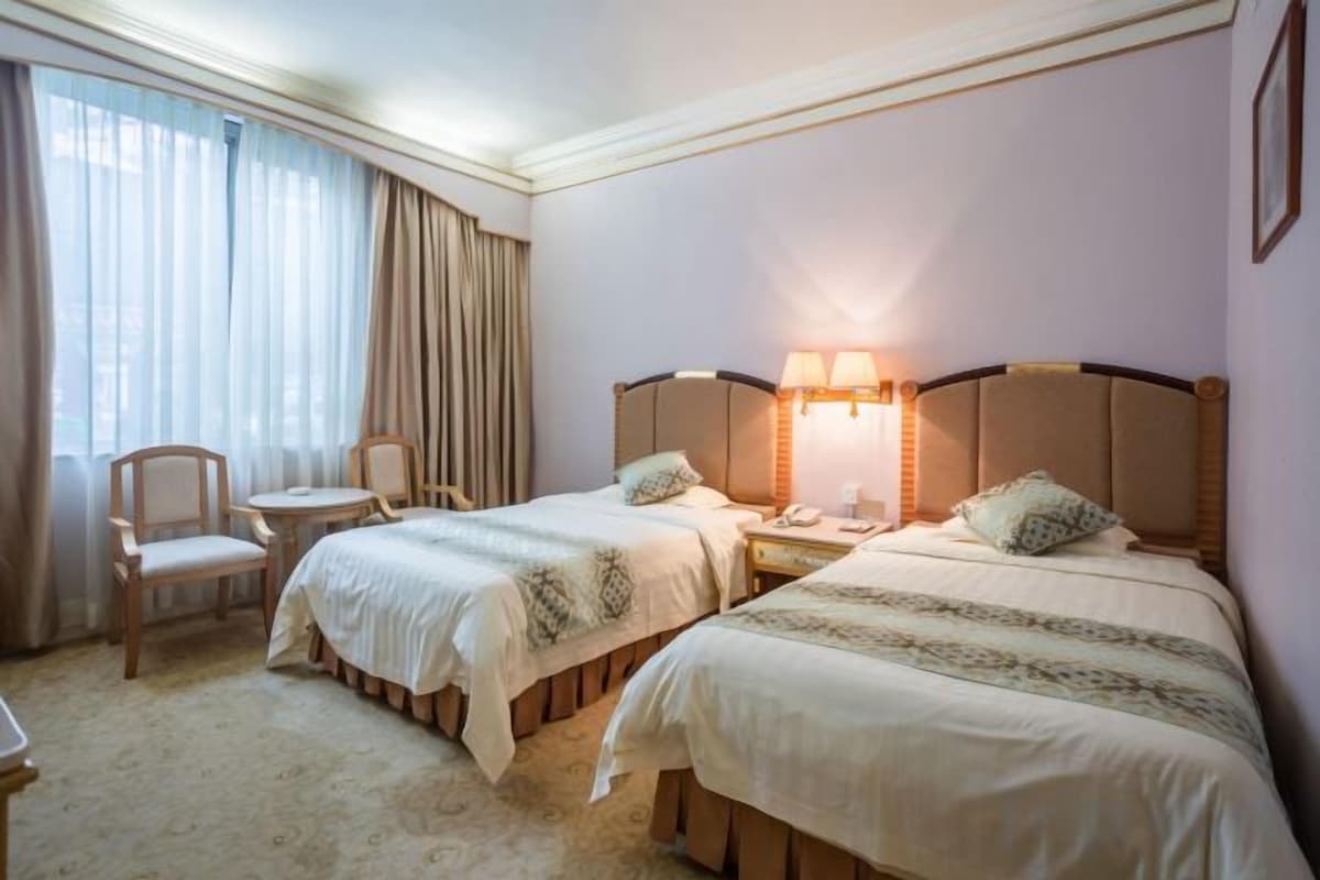 A hotel room with two beds, a desk, a chair, and a window with curtains.