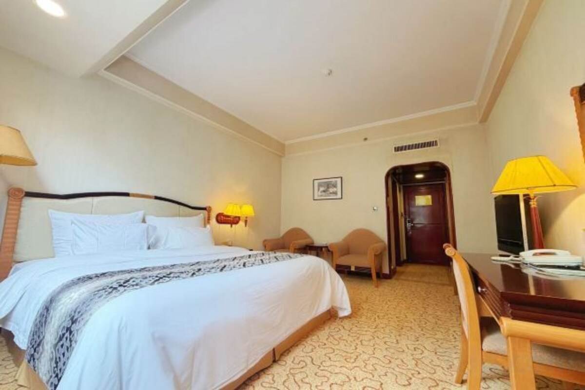 A hotel room with a bed, bedside table, lamp, and a desk with a chair.