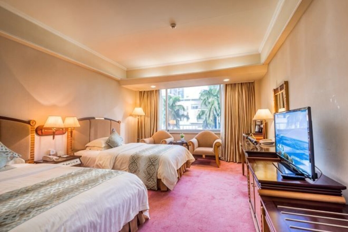 A hotel room with two beds, a TV, a desk, and a window with curtains.