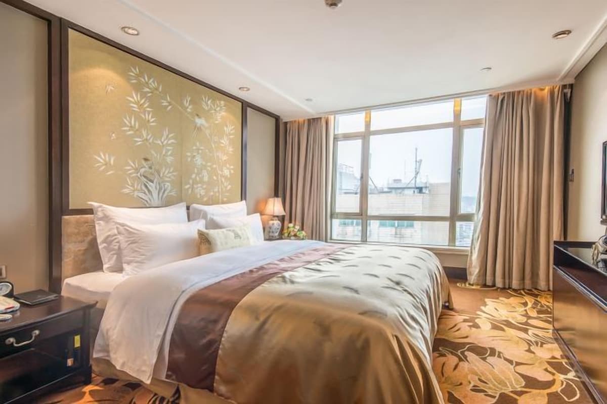 A hotel room with a large bed, a nightstand, a lamp, and a view of a bridge.