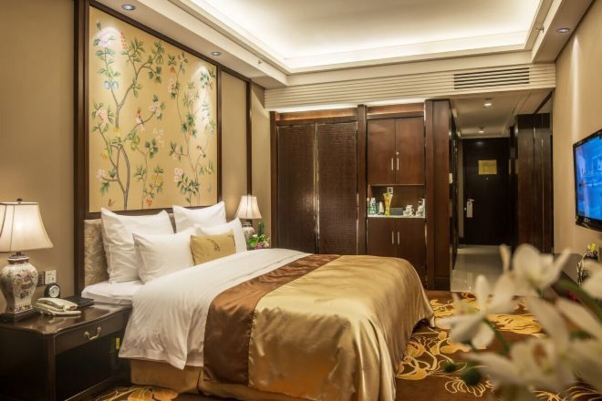 A hotel room with a large bed, a nightstand, a wall-mounted TV, and a wardrobe.
