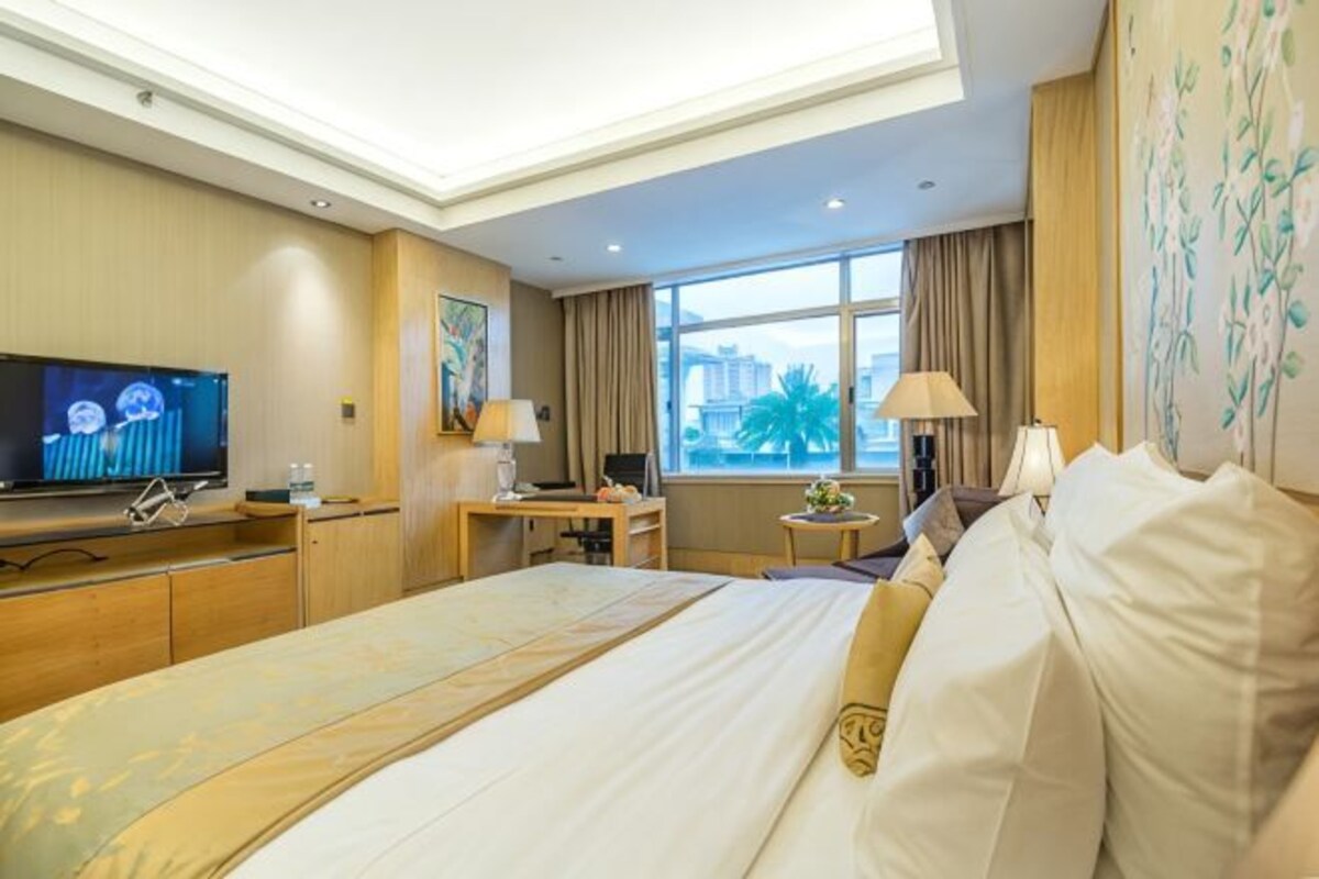 A hotel room with a large bed, a desk, a television, and a window with a view.