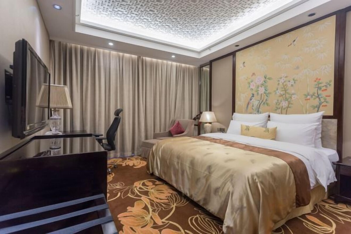A hotel room with a large bed, a desk, a chair, a TV, and a ceiling with a skylight.