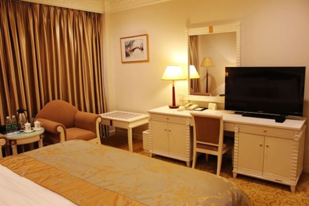 A hotel room with a bed, a desk with a lamp, a television, and a chair.