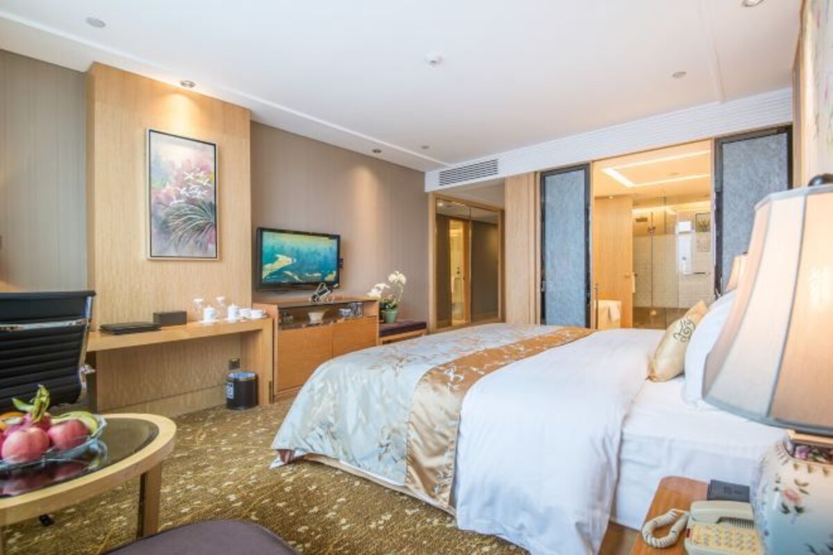 A hotel room with a bed, a desk, a television, and a bathroom visible through an open door.