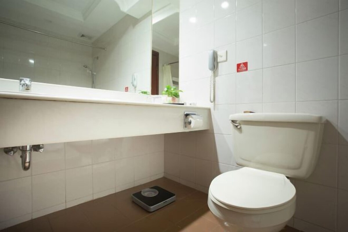 A bathroom with a white toilet, a sink with a mirror, and a scale on the floor.
