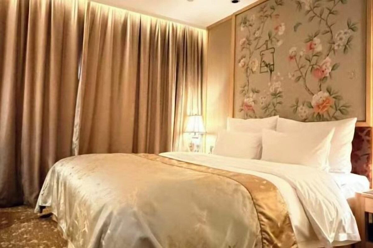 A hotel room with a bed, curtains, a floral wallpaper, and a nightstand.