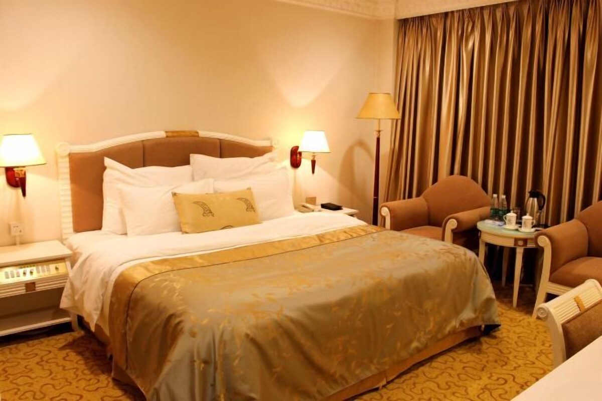 A hotel room with a large bed, two bedside tables with lamps, a chair, and a small table with a lamp.