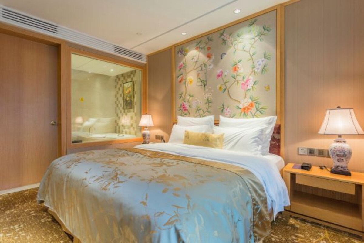 A hotel room with a large bed, a nightstand, a mirror, and a floral wallpaper.