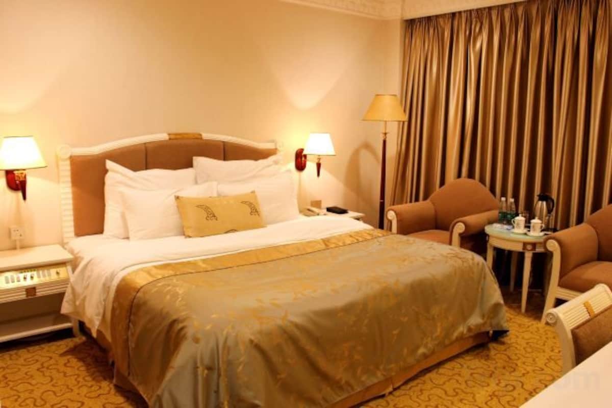 A hotel room with a bed, bedside lamps, a chair, a small table, and curtains.