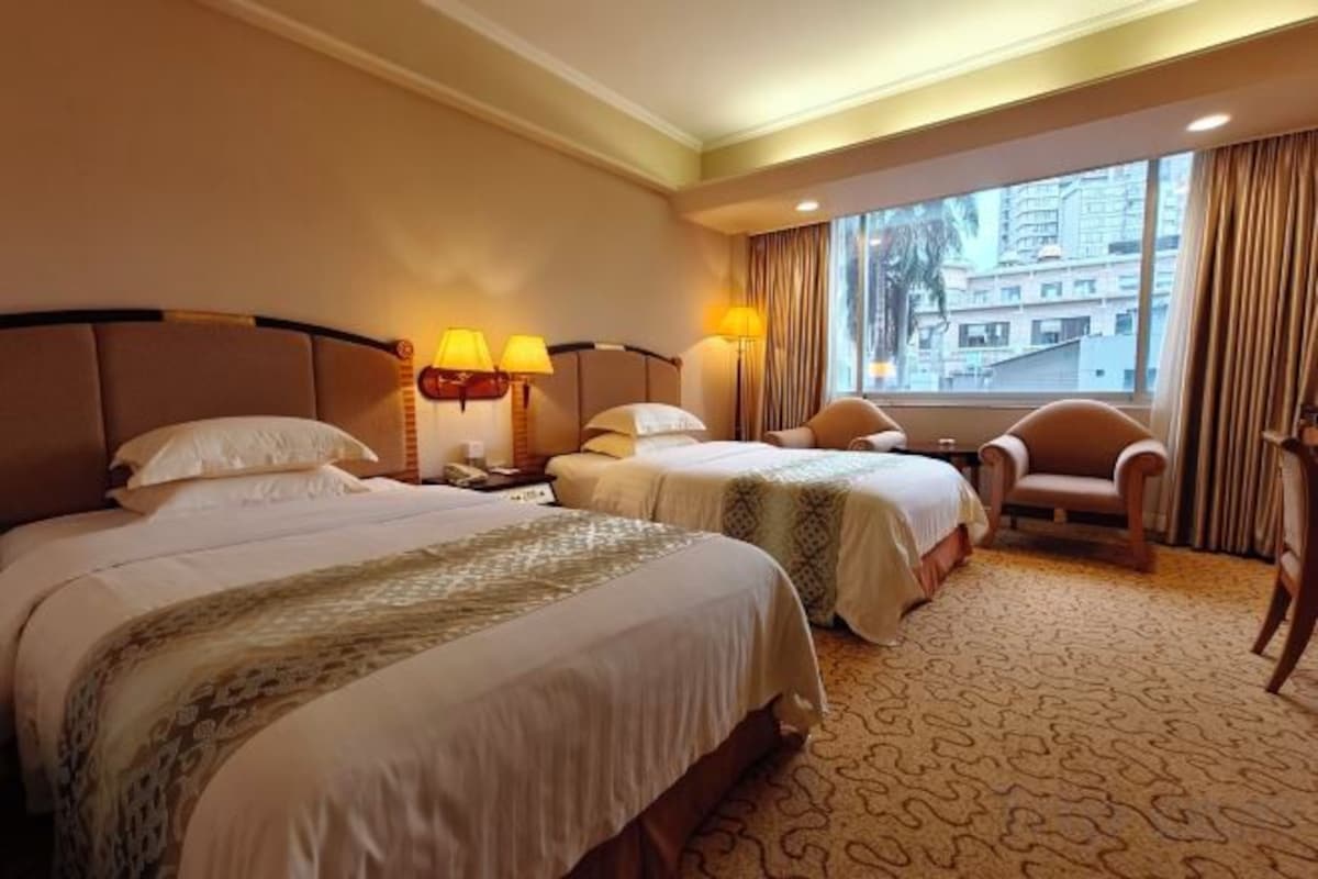 A hotel room with two beds, a window with curtains, a chair, and a lamp.