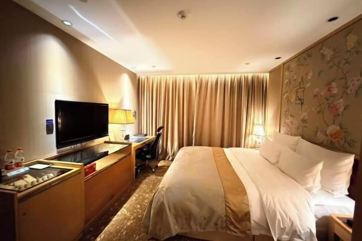 A hotel room with a bed, a desk with a computer, a television, and a window with curtains.