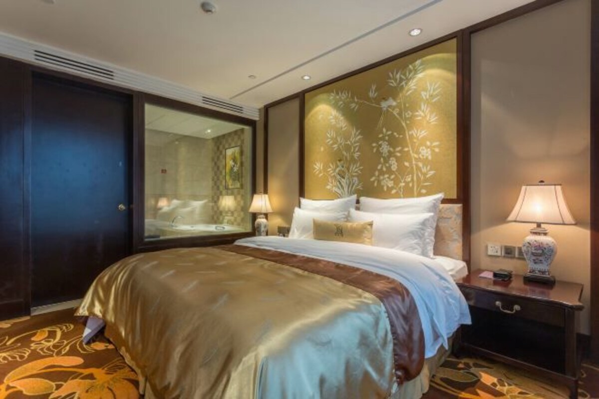 A hotel room with a large bed, a nightstand with a lamp, a mirror, and a floral wall panel.