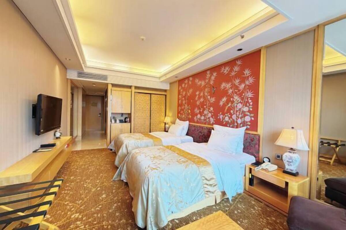 A hotel room with two beds, a TV, a desk, and a mirror.