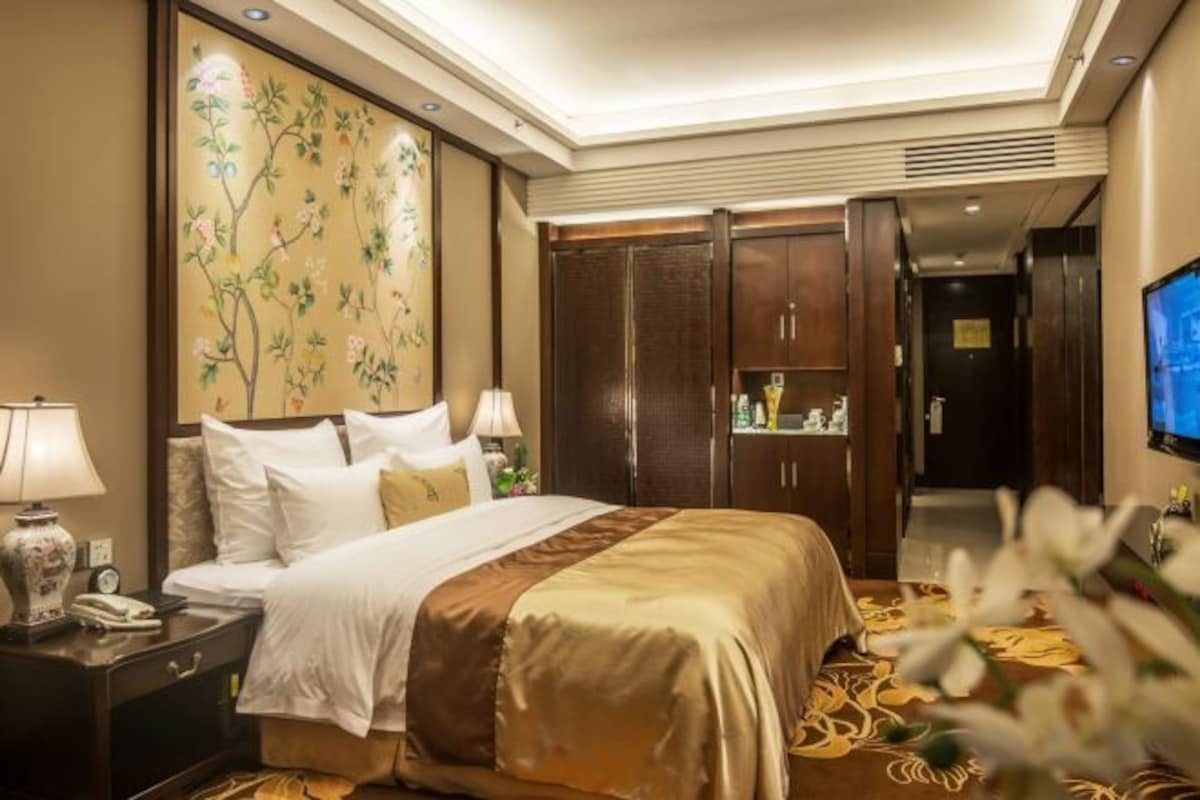 A hotel room with a bed, nightstand, lamp, artwork, wardrobe, and television.