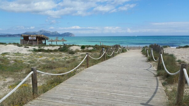 A wooden boardwalk leading to a beach area with thatched-roof structures and a clear view of the ocean. - Villa es Baulo Pleta, with garden and pool near beach (Can Picafort)