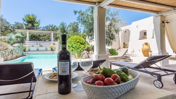 Un área junto a la piscina con una botella de vino, un cuenco de fruta y sillones de descanso.