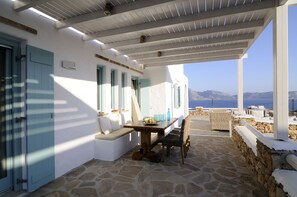 A covered outdoor seating area with stone flooring, white walls, and blue shutters. - 2 luxury villas complex with private pool, gym,spa & unrivalled view  (Koufonisia , Κουφονήσια)