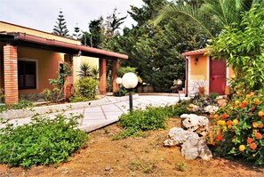A courtyard with a paved walkway, a small garden area with various plants, and a building with a red roof and brick walls. - Sunbay House 300 mt from Beach, Veranda Sea View (Balestrate)