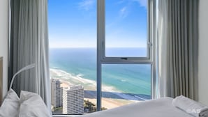 Quarto de hotel com uma grande janela que oferece vista para a praia e oceano.