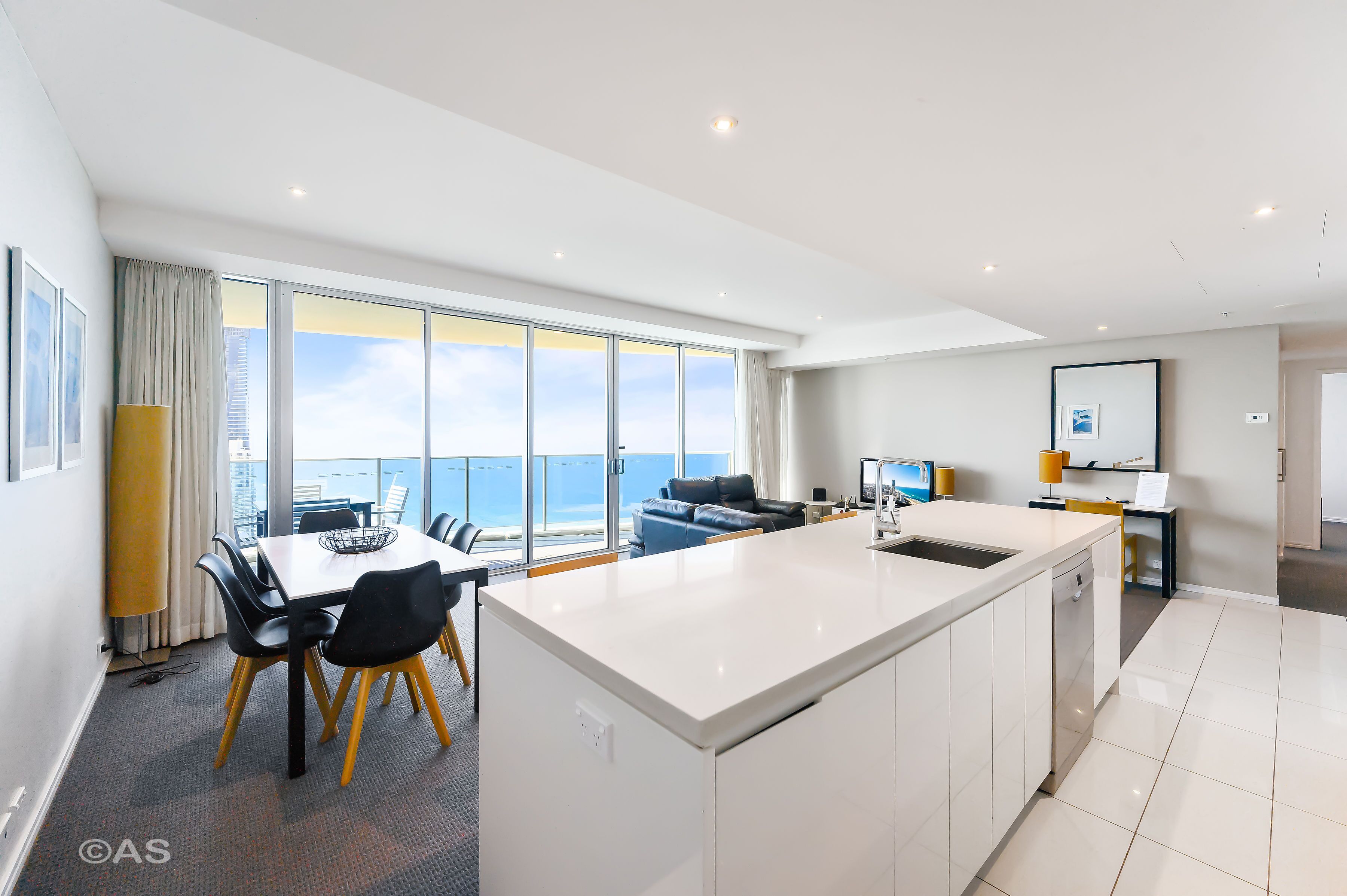 A modern kitchen with a large island, dining area with chairs, and a view of the sea through large windows.