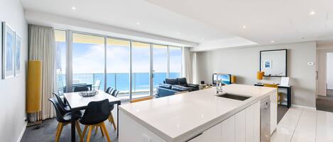A modern kitchen with a large island, dining area with chairs, and a view of the sea through large windows.