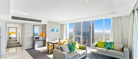 A modern hotel room with a dining area, a sofa set, and a large window offering a city view.